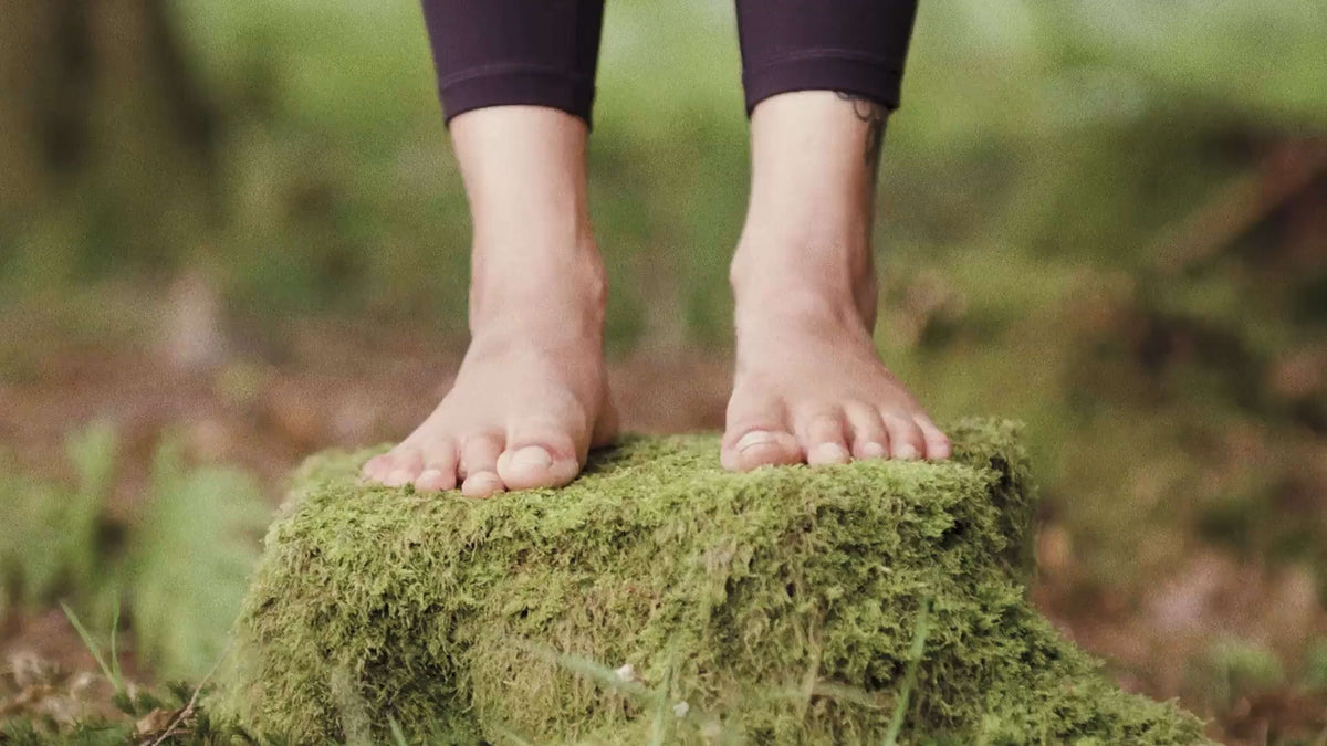 Bare feet standing on a moss-covered rock in nature